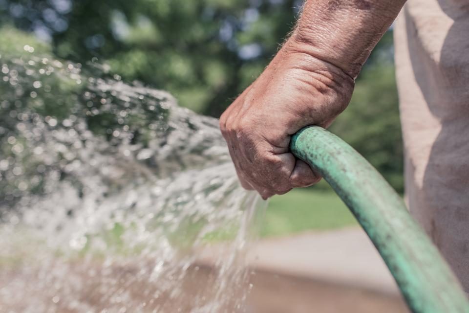 Eine Hand hält einen Gartenschlauch beim Bewässern